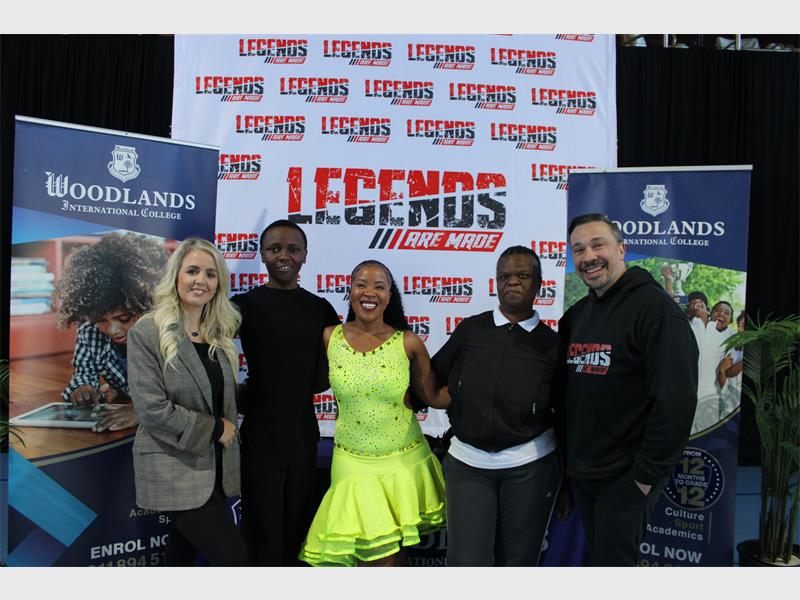 A white female and white male flanking three young black dancers, the female wearing a flowing yellow dress and all in front of a banner reading Legends are Made.