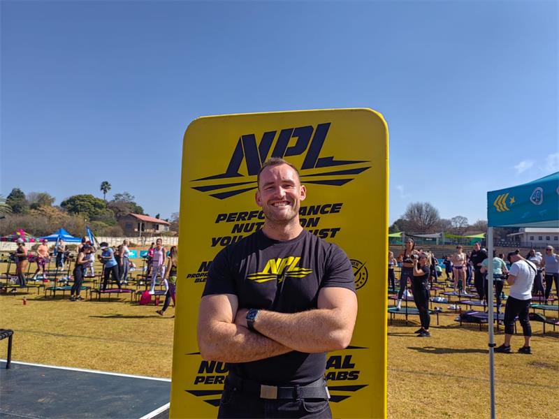 A white male with his arms crossed in front of a yellow banner, wearing a black T-shirt.