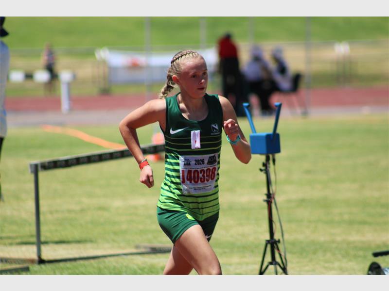 A female athlete in motion on a running track wearing green kit.