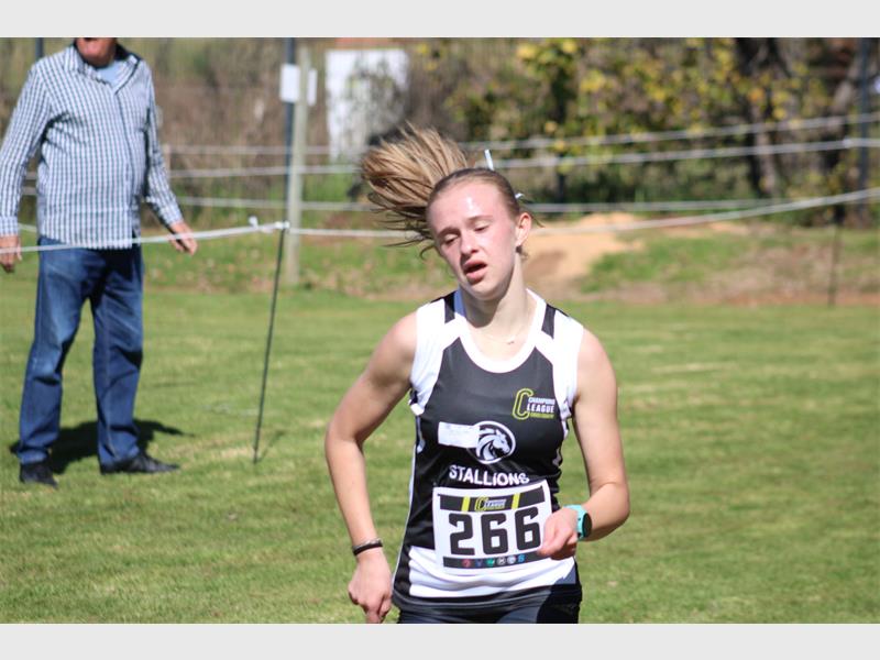 A young female athlete with her blonde ponytail blowing in the wind pictured during a race, wearing blue and white kit.