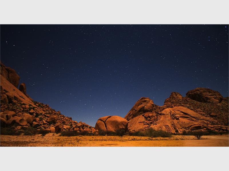 A photo of a barren landscape of desert and rock with a starry night sky in the background. 