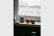 Cups and fruit on a cupboard in front of a window that depicts moisture drops on the outside.