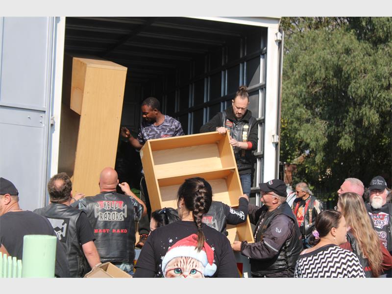 People in the back of a big truck off loading wooden shelves to people standing waiting to assist them.
