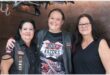 Three female members of Hell Razors biker club standing next to each other smiling for the camera, all dressed in the club's shirts and jackets.