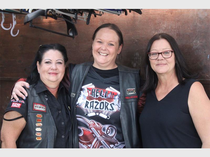Three female members of Hell Razors biker club standing next to each other smiling for the camera, all dressed in the club's shirts and jackets.
