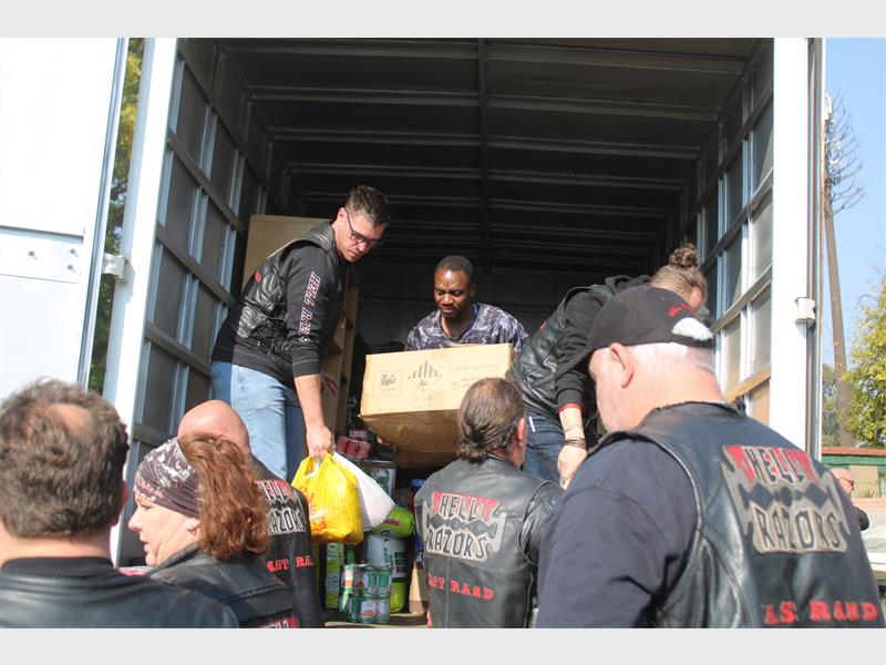 Members of a biker club off load donations from the back of a big truck for residents of a caravan park.
