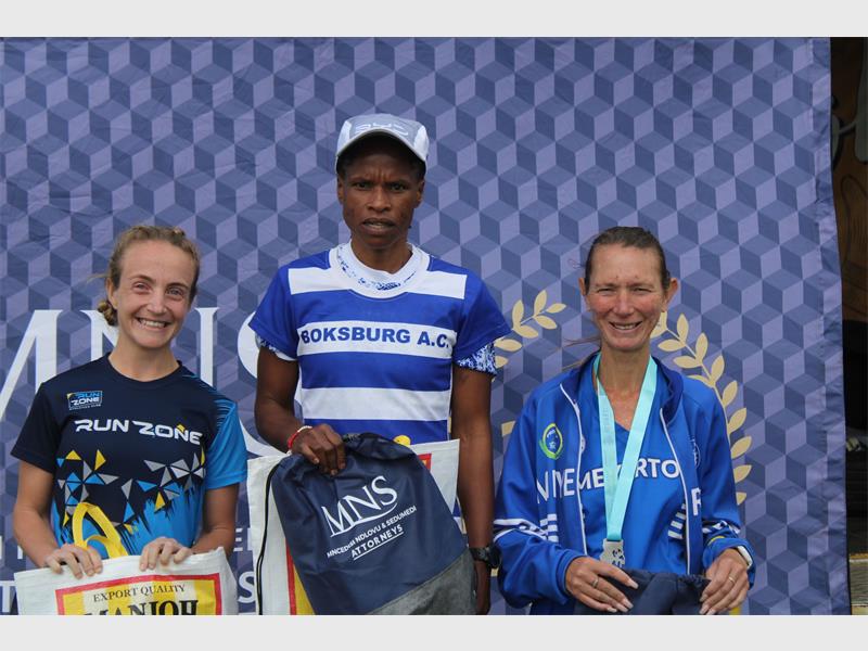 Two white woman and a black woman on a podium after a marathon.