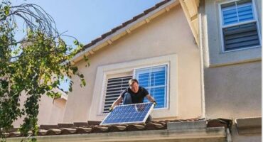 Image of a man standing on a roof holding a solar panel