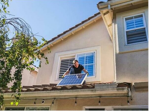 Image of a man standing on a roof holding a solar panel