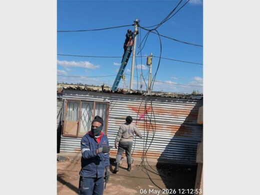 One officer working from a ladder to cut cables feeding the informal structures.