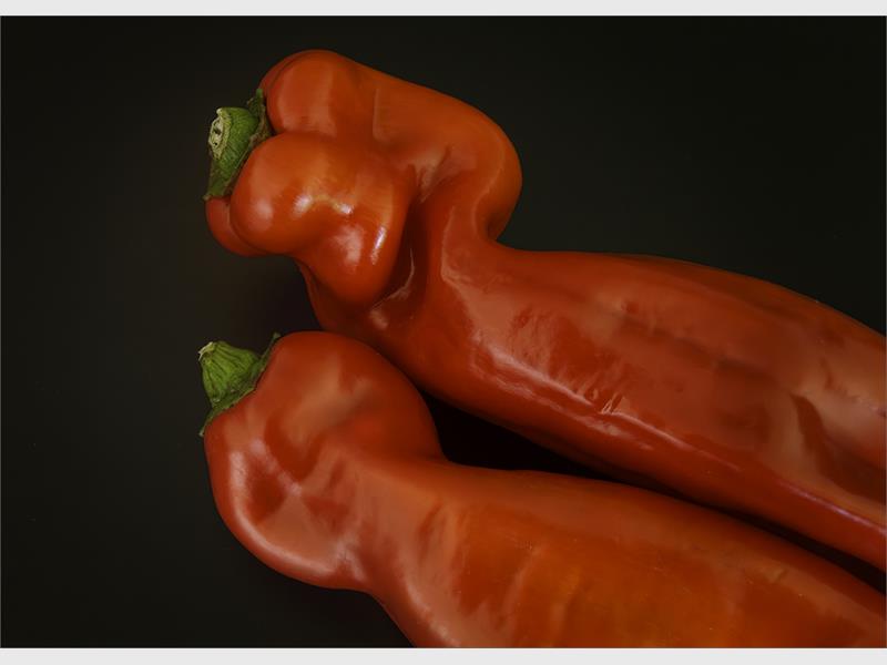 Two odd shaped red peppers with green tops lying next to each other.