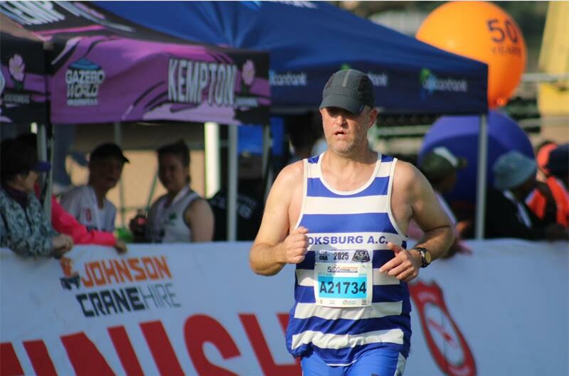 A white male athlete in BAC kit and wearing a blue cap competing in the Comrades Marathon.