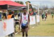 A young black athlete standing on grass next to banners at the end of a marathon event.