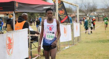 A young black athlete standing on grass next to banners at the end of a marathon event.