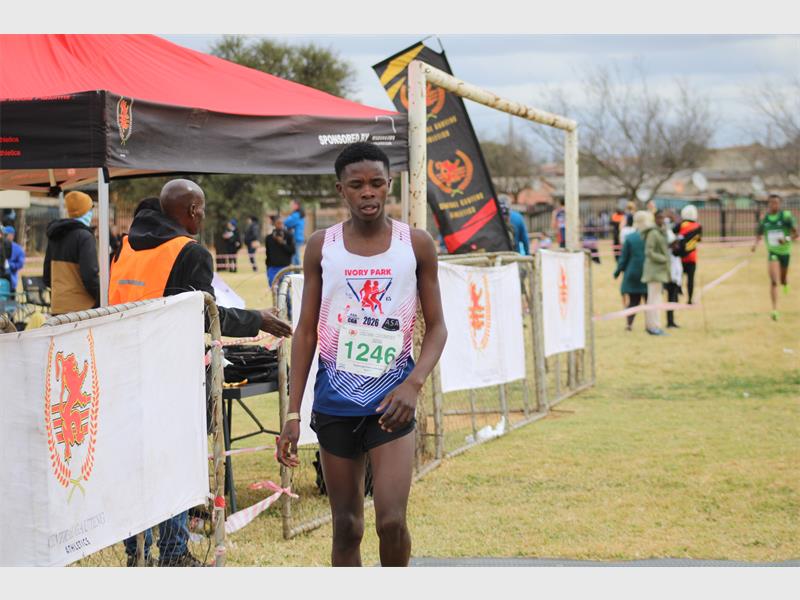 A young black athlete standing on grass next to banners at the end of a marathon event.