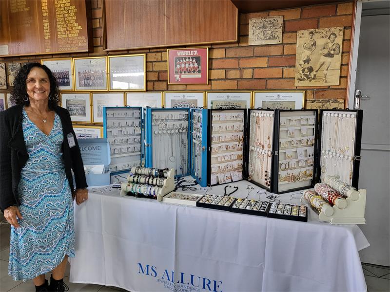 A woman in a blue dress standing next to a table displayed full of jewellery on display stands.
