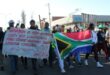 Group of protesters holding a South African flag and a hand written poster