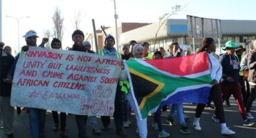 Group of protesters holding a South African flag and a hand written poster