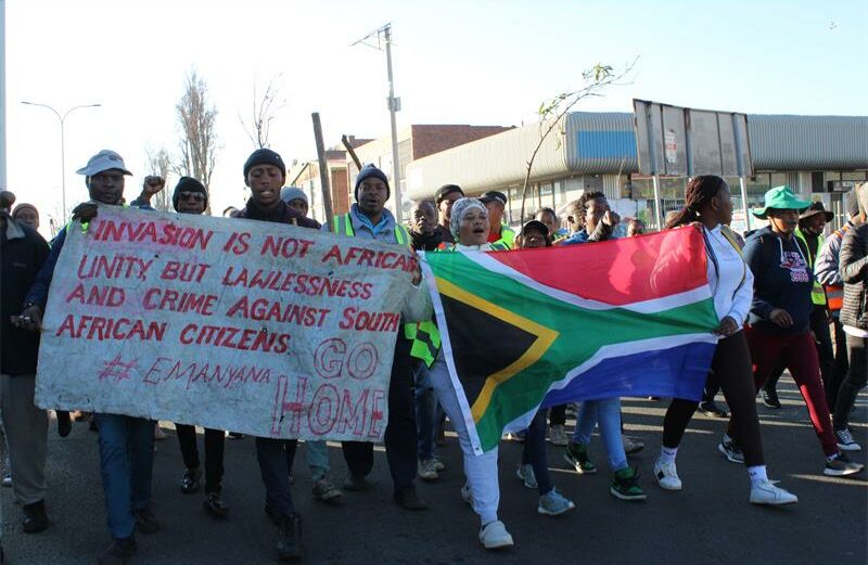 Group of protesters holding a South African flag and a hand written poster