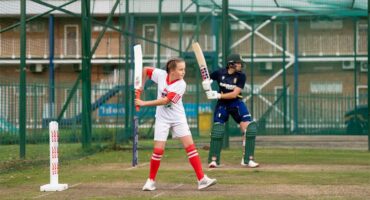 A junior and adult cricket player batting in the nets during a training session.