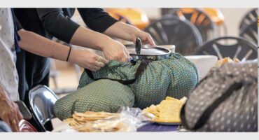 Wonderbag slow cookers on a table with hands reaching in to secure them for the cooking process.