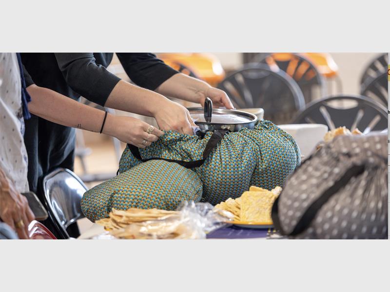 Wonderbag slow cookers on a table with hands reaching in to secure them for the cooking process.