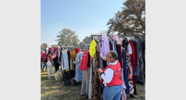 A woman standing next to rails of clothing for the needy at an outreach event.