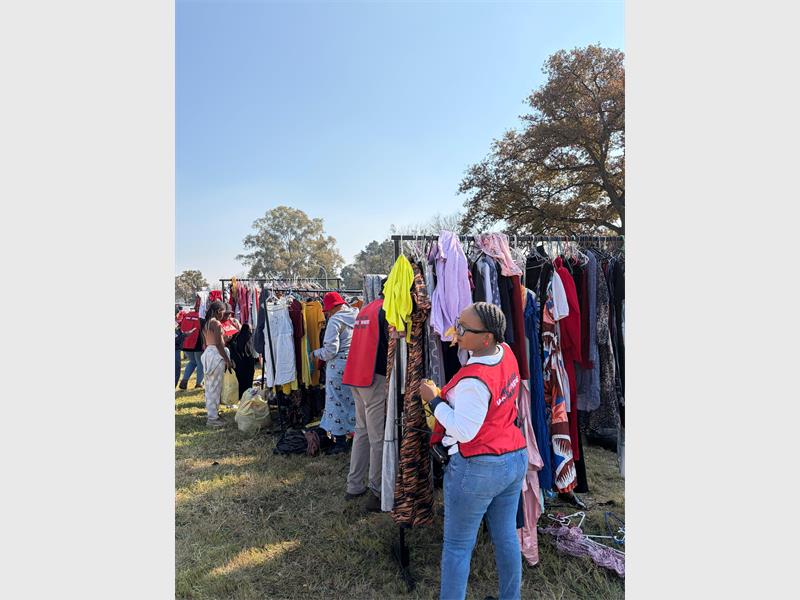 A woman standing next to rails of clothing for the needy at an outreach event.