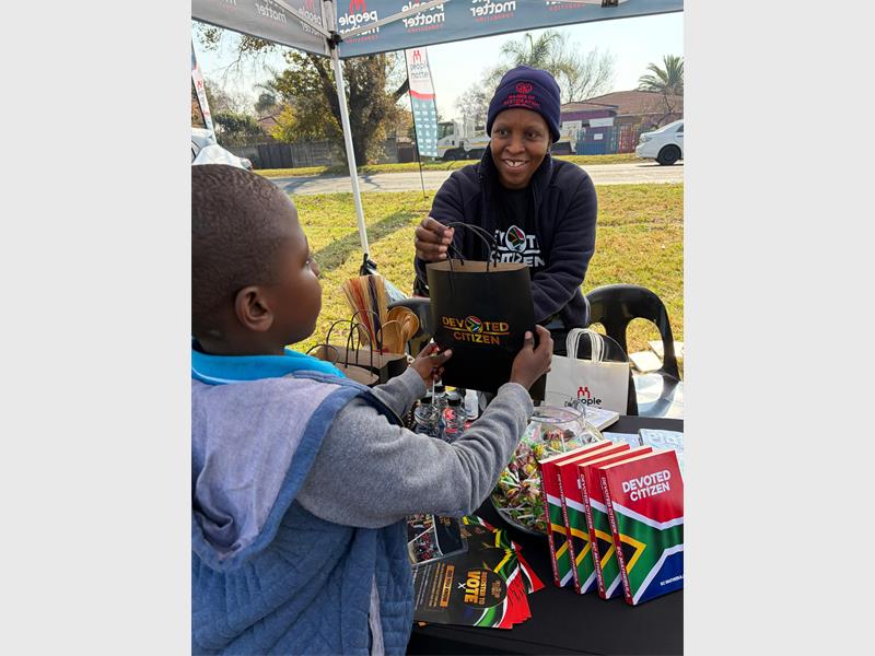 A black woman hands a small black child a package from a table.