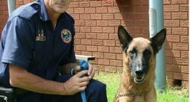 Man in a police uniform kneeling next to a dog