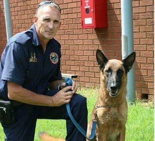 Man in a police uniform kneeling next to a dog