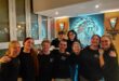 Nine young men and women dressed in black shirts standing in a row with a Spur logo in the background.