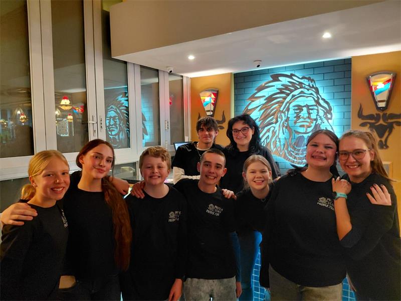Nine young men and women dressed in black shirts standing in a row with a Spur logo in the background.