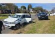 A crime scene showing a white bakkie and a darker bakkie in the background parked on the side of a road with the white bakkie's back doors open.