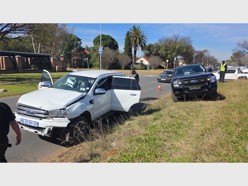 A crime scene showing a white bakkie and a darker bakkie in the background parked on the side of a road with the white bakkie's back doors open.