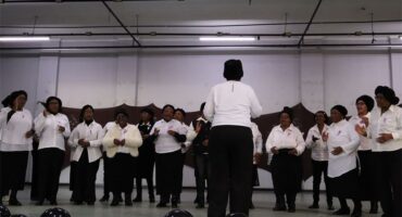 A choir of elderly women dressed in black and white on stage.