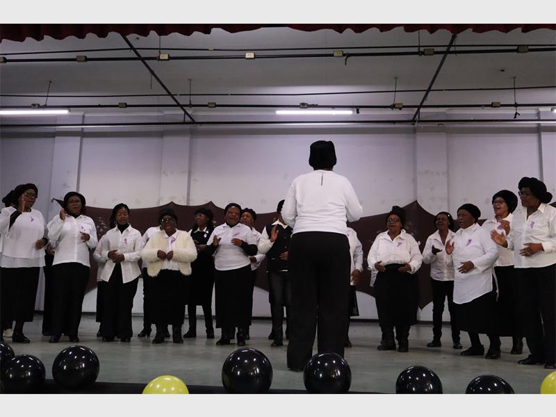 A choir of elderly women dressed in black and white on stage.