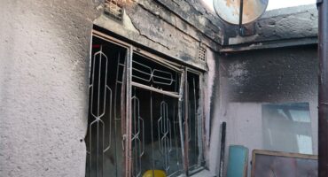 The burnt remains of a home photographed from the outside showing a window frame.