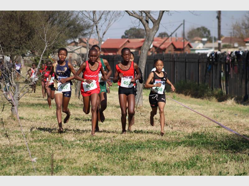 A group of young black athletes dressed in red and some in black running on a grass track.
