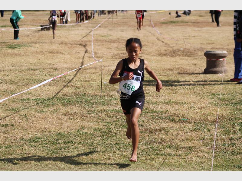 A young black female athlete dressed in black kit running on a grass track towards the finish line.