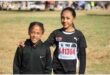 Two young black female athletes one with an arm around the other and both dressed in black kit.