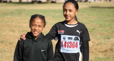 Two young black female athletes one with an arm around the other and both dressed in black kit.
