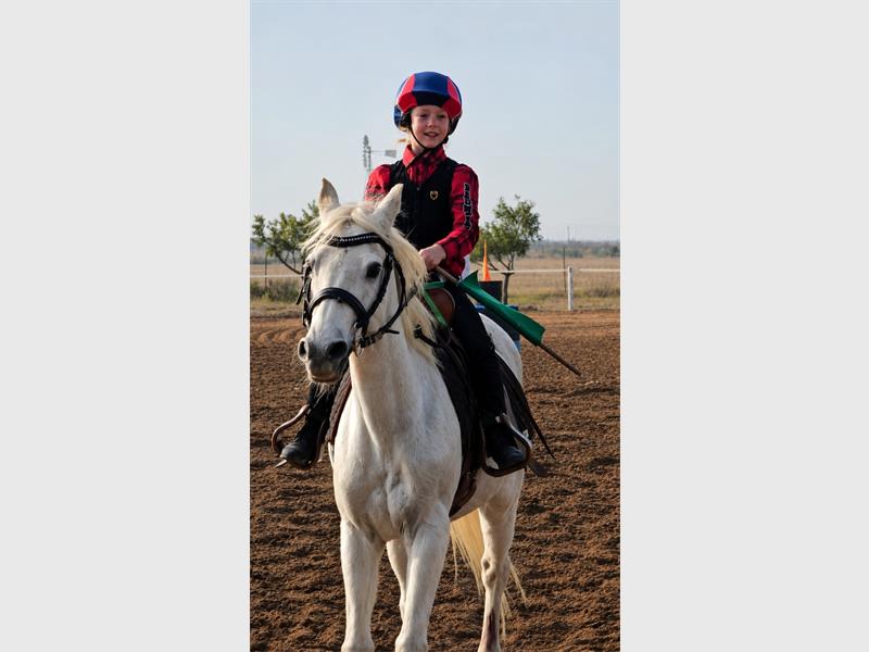 A young rider on a white horse wearing red and blue shirt and red and blue helmet.