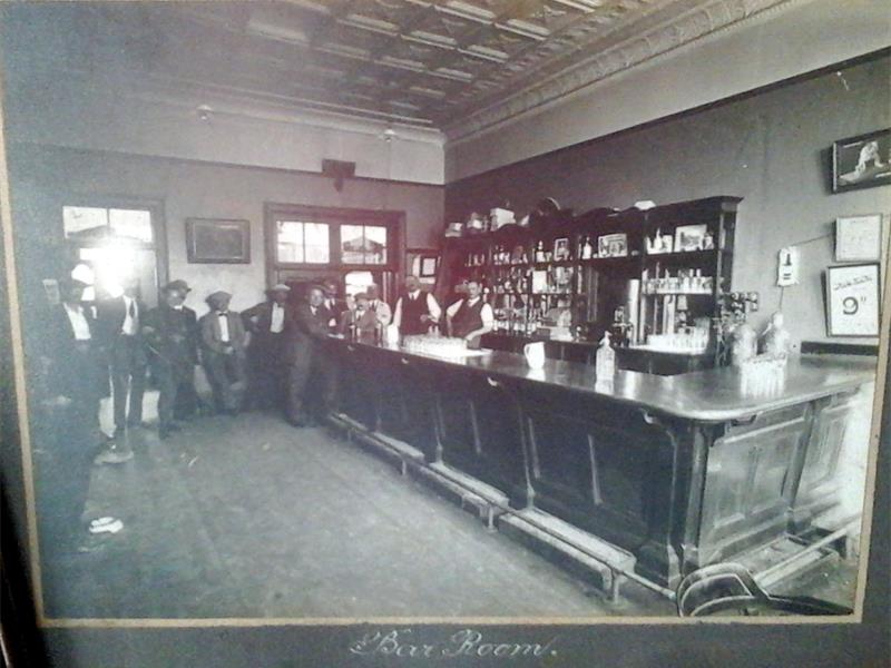 A black and white image of a bar with several men standing in one corner.