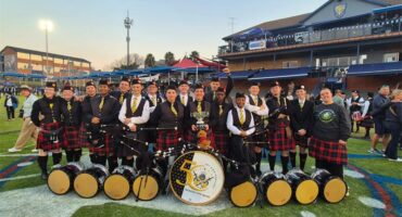 Pipe band members posing with a trophy and their instruments