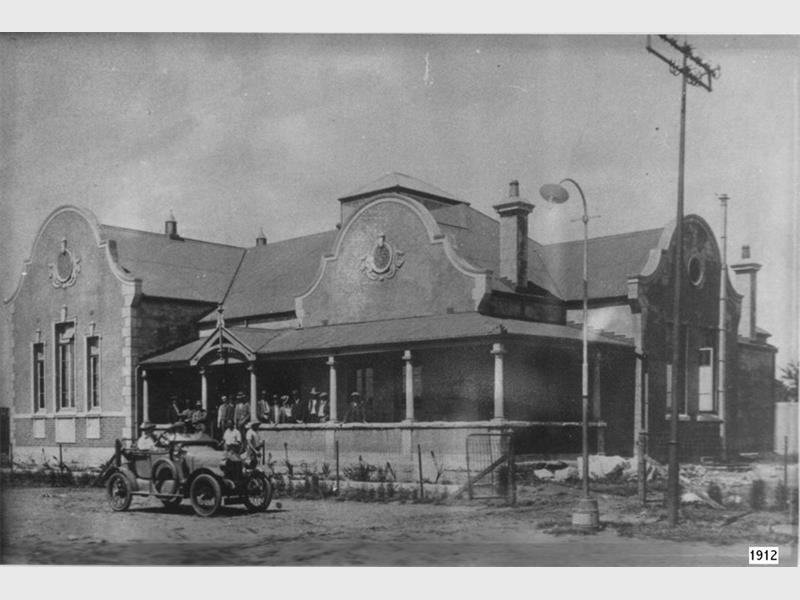 A black and white image of an old building with an old car parked outside.