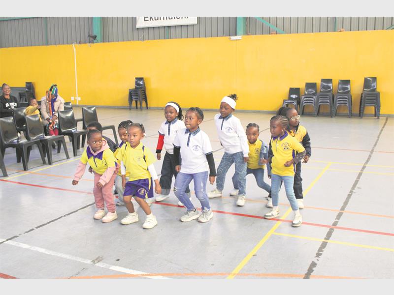 A group of ECD learners doing a dance on the floor in a hall. 
