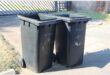 Two black City of Ekurhuleni wheelie bins next to each other.