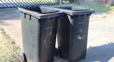 Two black City of Ekurhuleni wheelie bins next to each other.