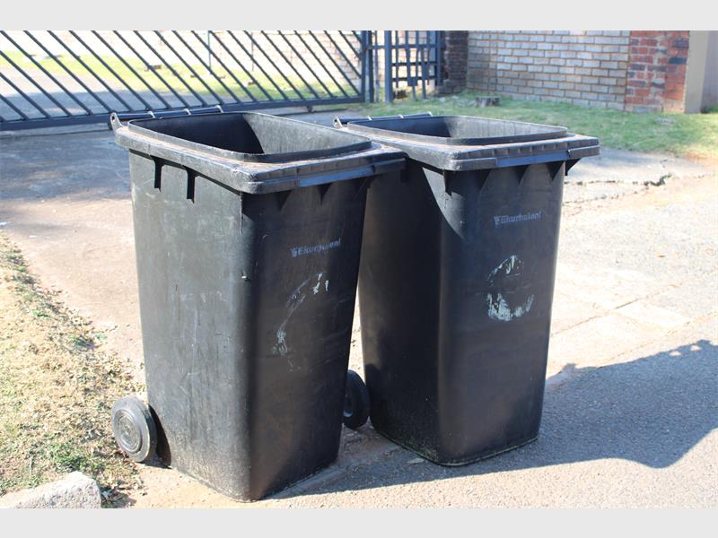 Two black City of Ekurhuleni wheelie bins next to each other.